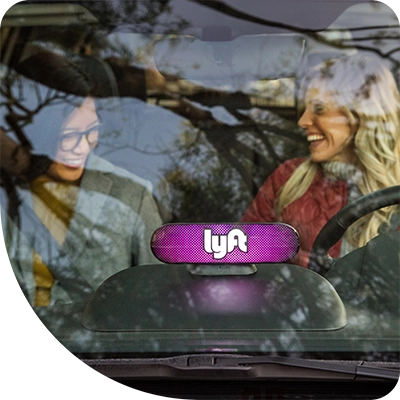 Two people are smiling inside a car with a Lyft logo device visible on the dashboard.
