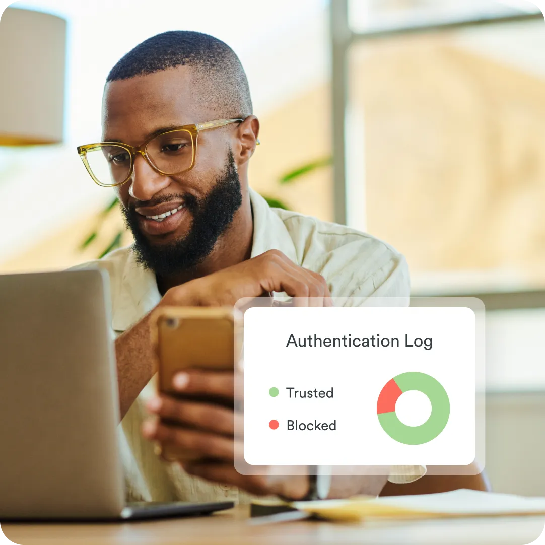Smiling professional in glasses holding phone up and seeing authentication log in the foreground showing Duo's MFA with trusted and blocked authentication attempts.