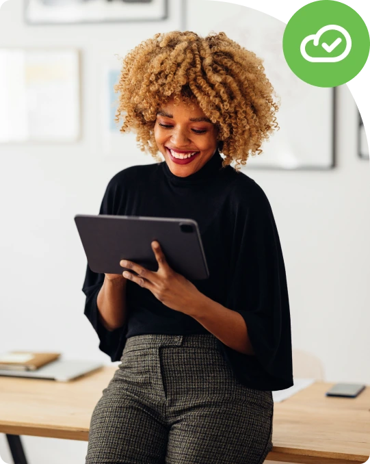 Person on desk with tablet, cloud check icon in corner.