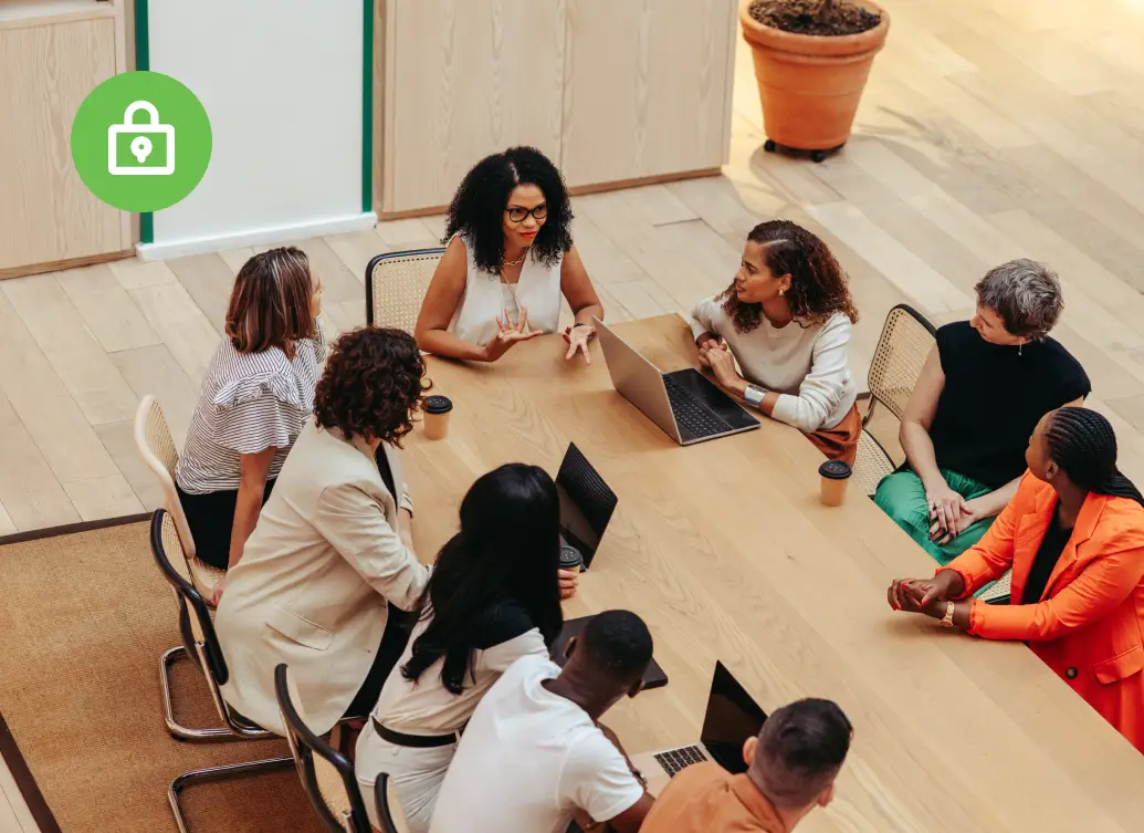 Professionals gathered around a conference table discussing ideas, with laptops and coffee cups visible in a modern office
